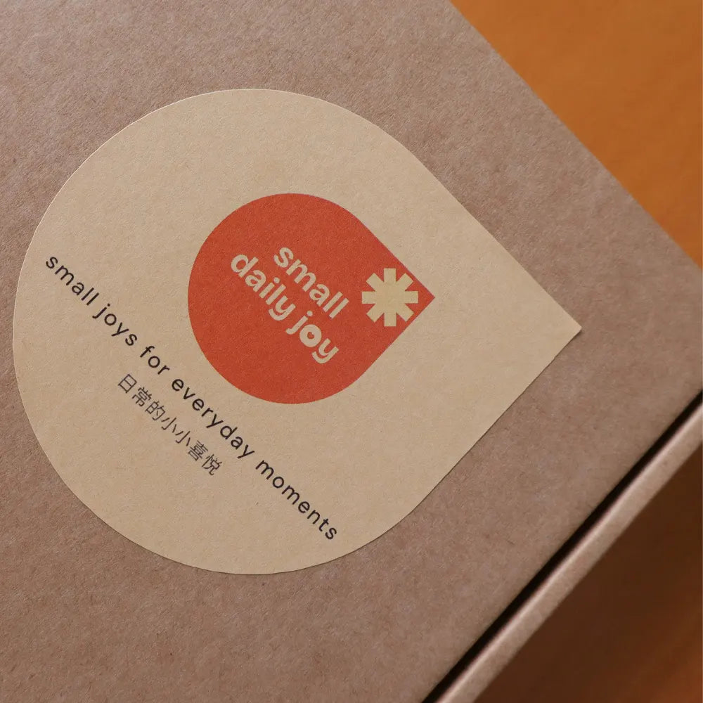 A kraft paper packaging box with a die-cut Small Daily Joy logo label.